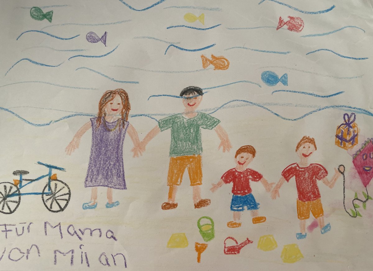 Dečji crtež: porodica ruku pod ruku na plaži, sa ribicama, biciklom i zmajem; u uglu rukom piše „Für Mama von Milan“ – Za mamu, od Milana